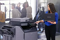 Sharp copier in an office being used by somone holding a laptop